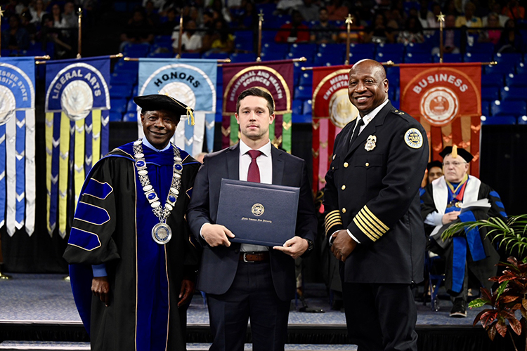 Metro Nashville Police Department detective Michael Collazo, center, holds his honorary professorship in public safety certificate presented by MTSU President Sidney A. McPhee, left, at the university’s spring commencement ceremony Friday, May 5, in Murfreesboro, Tenn. At right is Metro Nashville Police Chief John Drake. A total of five officers received the honor for their heroic response to the Covenant School shooting in Nashville, Tenn., in late March. (MTSU photo by James Cessna)