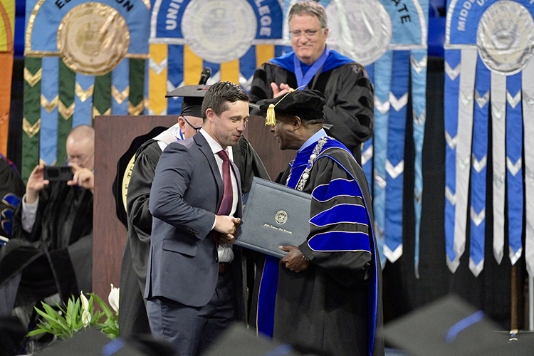 Metro Nashville Police Department detective Michael Collazo, left, accepts his honorary professorship in public safety certificate from MTSU President Sidney A. McPhee at the university’s spring commencement ceremony Friday, May 5, in Murfreesboro, Tenn. Applauding on stage is University Provost Mark Byrnes. A total of five officers received the honor for their heroic response to the Covenant School shooting in Nashville, Tenn., in late March. (MTSU photo by Andy Heidt)
