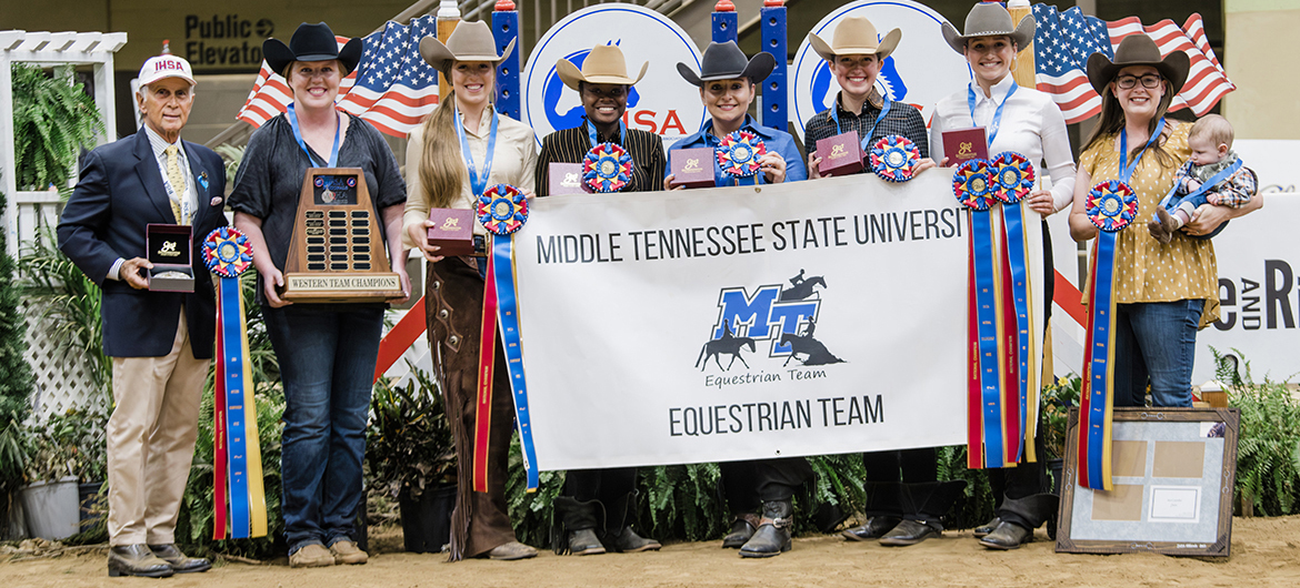 Joined by Intercollegiate Horse Shows Association founder Bob Caccione, left, and with their individual awards and the IHSA Western Team Champions trophy, Middle Tennessee State University equestrian team members include, from left, coach Ariel Higgins, Audrey Ferrie, Sadio Barnes, Mackenzie Latimer, Jordan Martin, Jessie Kauffman and assistant coach Andrea Rego, holding Levi Rego, during closing ceremonies at the event at Kentucky Horse Park in Lexington, Ky. (Photo by EQ Media)