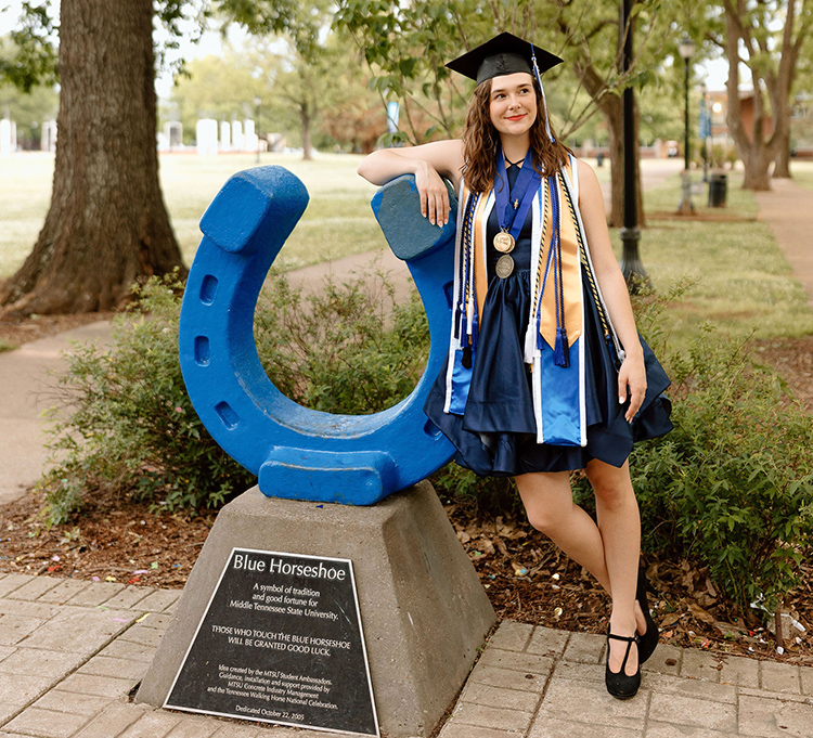 In this spring photo, Catheryn Bolick, a spring Middle Tennessee State University Honors College graduate from Smyrna, Tenn., leans on the blue horseshoe in Walnut Grove wearing her mortarboard and academic stoles and cords. Bolick is one of 62 recipients nationwide to receive Phi Kappa Phi Fellowship for 2023. (Submitted photo)