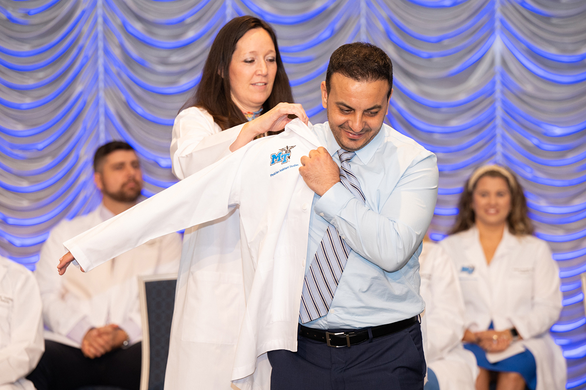 MTSU Physician Assistant Studies Director Marie Patterson helps student Muhamed Faour put on his clinician's coat at the inaugural “white coat” ceremony held Aug. 11, 2023, in the Student Union Ballroom at Middle Tennessee State University. (MTSU photo by James Cessna)
