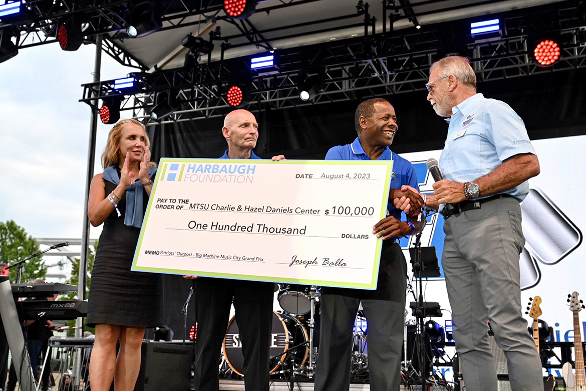 From right, Harbaugh Foundation Director Joe Balla presents a $100,000 check to MTSU President Sidney A. McPhee, retired Army Lt. Gen. Keith Huber, MTSU senior adviser for veterans and leadership initiatives, and Daniels Veterans Center Director Hilary Miller Friday, Aug. 4, at the Big Machine Music City Grand Prix in downtown Nashville, Tenn. (MTSU photo by James Cessna)