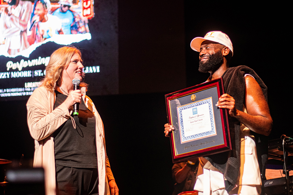 Middle Tennessee State University alumnus and independent hip-hop artist Tyrone “Tyke T” Stroble, right, is all smiles after being surprised by MTSU College of Media and Entertainment Beverly Keel, left, who presented him with a framed honorary professorship certificate on Sept. 17 during a break in his special concert at the Orpheum Theatre in Memphis, Tenn. The Smyrna, Tenn., native earned his bachelor’s and MBA degrees from MTSU. (Courtesy of Amiya Samaar)