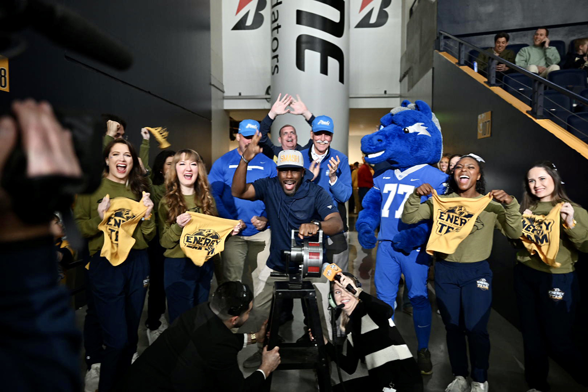 With cheerleading help, Derek Mason, center, Middle Tennessee State University Blue Raiders football coach, rides the elliptical machine during the Preds True Blue Night/Military Appreciation event during the NHL Nashville Predators' game March 19 against the San Jose Sharks at Bridgestone Arena in Nashville, Tenn. Mason served as a fan captain before the start of the game. (MTSU photo by James Cessna)