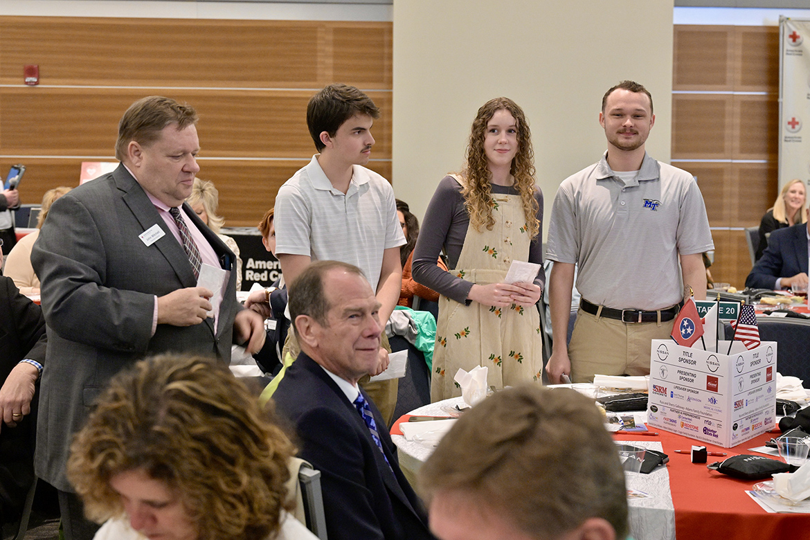 Standing, from left, John Mitchell, executive director of the American Red Cross Heart of Tennessee Chapter, makes a special presentation to MTSU Campus Recreation student workers Andrew Scrugham, Julia Rutledge and Gatlin Murr on March 5, 2024, during the chapter’s “Heroes Luncheon” at the MTSU Student Union Ballroom in Murfreesboro, Tenn. The students were recognized for their life-saving emergency response to cardiac arrest survivor and retired MTSU professor Richard Detmer, seated at center. (MTSU photo by Andy Heidt)