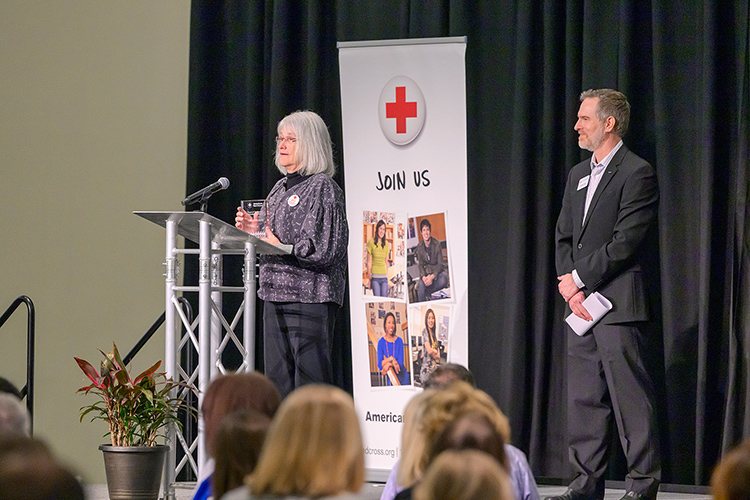 Retired Middle Tennessee State University electronic media communication professor Mary Nichols, left, gives remarks after being presented the Volunteer Spotlight Award during the American Red Cross Heart of Tennessee Chapter’s “Heroes Luncheon” on March 5, 2024, at the MTSU Student Union Ballroom. At right is Jonathan Taylor, Red Cross Disaster Program manager, who presented the award. (MTSU photo by Andy Heidt)