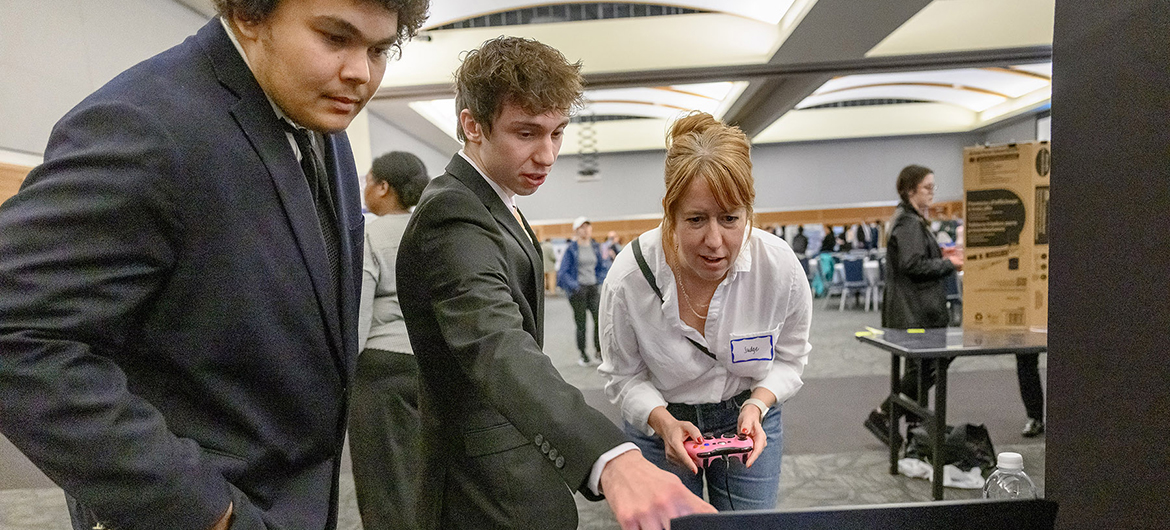 Middle Tennessee State University interactive media seniors Jacob Moore, left, and Josiah Parkhurst, center, demonstrate their accessible video game project to Kristine Potter, assistant professor, one of the around 176 projects at the 18th annual Scholars Week student research and creative activity exposition on March 15, 2024, in the Student Union ballroom on campus in Murfreesboro, Tenn. (MTSU photo by J. Intintoli)