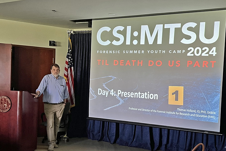 Tom Holland, director of the Forensic Institute for Research and Education at Middle Tennessee State University, is shown inside an MTSU Honors Building classroom next to a presentation slide for the 2024 CSI: MTSU Forensic Summer Youth Camp, held recently at Middle Tennessee State University in Murfreesboro, Tenn., and carrying the title of “Til Death Do Us Part.” MTSU hosted 32 high school students for the annual event. (Submitted photo)