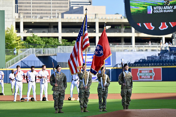 As Nashville Sounds players look on in the background, four cadets with the Middle Tennessee State University Army ROTC present the colors before the Sounds’ special Military Appreciation Night game Thursday, June 6, at First Horizon Park in Nashville, Tenn. Sounds players are wearing special military-themed jerseys that are being auctioned to benefit MTSU’s Charlie and Hazel Daniels Veterans and Military Family Center. (MTSU photo by James Cessna)