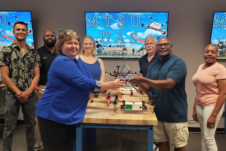 Carol Swayze, front left, Experiential Learning Program director at Middle Tennessee State University, presents Daryl Hickman Sr., front right, the 2023-24 EXL Outstanding Community Partner Award inside Middle Tennessee State University’s Unmanned Aircraft Systems Operations department in the Business and Aerospace Building on MTSU’s campus in Murfreesboro, Tenn. Also pictured, second row from left, are Daryl Hickman III, Daryl Hickman, II, UAS Lab Manager Felicia Davis, and UAS Program Director Kevin Corns, and Hickman Sr.’s wife, Lisa Hickman. (Submitted photo)