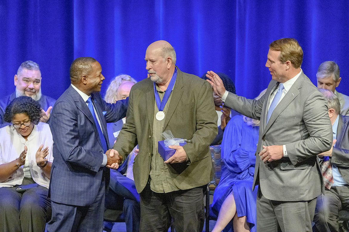 Middle Tennessee State University aerospace professor Paul Craig, center, shakes hands with university President Sidney A. McPhee, left, after accepting the MTSU Foundation’s Career Achievement Award at the 2024 Fall Faculty and Staff Meeting held Thursday, Aug. 22, inside Tucker Theatre on the MTSU campus in Murfreesboro, Tenn. At right is MTSU Foundation President Brian Kidd. (MTSU photo by Andy Heidt)