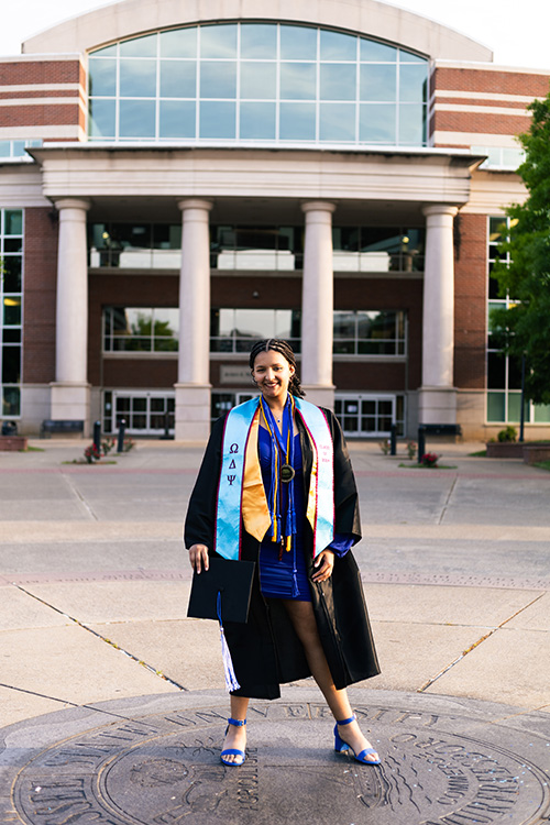 Middle Tennessee State University alumna and recording industry graduate Liliana Manyara stands on the engraved university seal located near James E. Walker Library while posing for graduation photos on campus in Murfreesboro, Tenn. (Photo submitted)