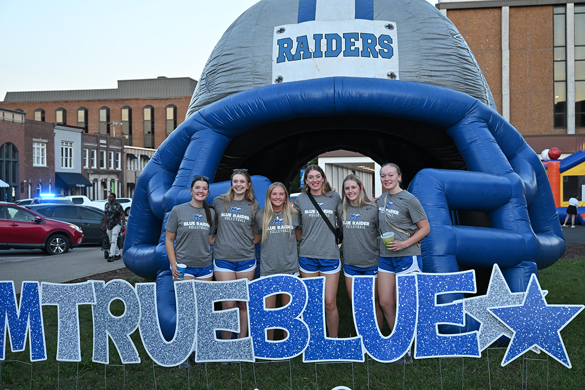 Some members of the Middle Tennessee State University volleyball team pose with a Blue Raider Football-branded, helmet-shaped bounce house and an “I Am True Blue” sign at the October Friday Night Live concert in downtown Murfreesboro, Tenn. The event featuring MT Athletics was cosponsored by the university as part of a growing partnership with the Main Street Murfreesboro downtown advocacy organization. (MTSU photo by James Cessna)