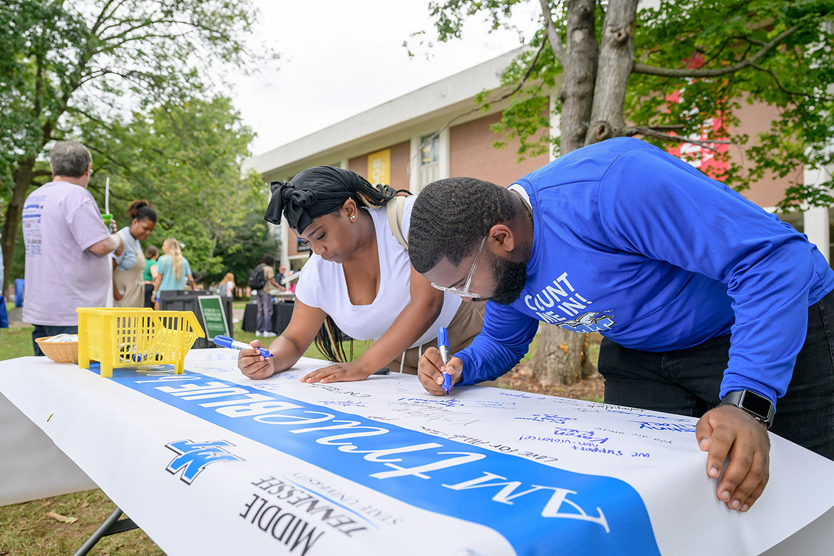 Michai Mosby, right, president of the Student Government Association at Middle Tennessee State University, signs the Campus Nonviolence Committee’s banner that reaffirms the True Blue Pledge of committing to reason and not violence at the annual International Day of Nonviolence event Wednesday Oct. 2, in Walnut Grove in Murfreesboro, Tenn. (MTSU photo by J. Intintoli)