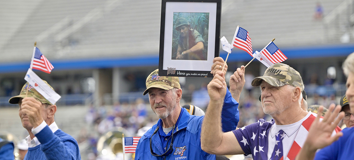 Middle Tennessee State University alumnus and U.S. Army Veteran Bob Lamb (Classes of 1969 and ’77), center, of Murfreesboro, Tenn., walks across Horace Jones Field in Floyd Stadium in Murfreesboro carrying a framed photo of his longtime friend and veteran, Bud Morris (’69, ’75)), Saturday, Nov. 9, during the 42nd annual MTSU Salute to Veterans and Armed Forces game during the halftime parade by service branches to theme songs performed by the Band of Blue. Morris, who attended the game, saluted his friends and fellow vets from the Jeff Hendrix Stadium Club, the first time in 40 years he has not walked with his military brothers and sisters. (MTSU photo by Andy Heidt)