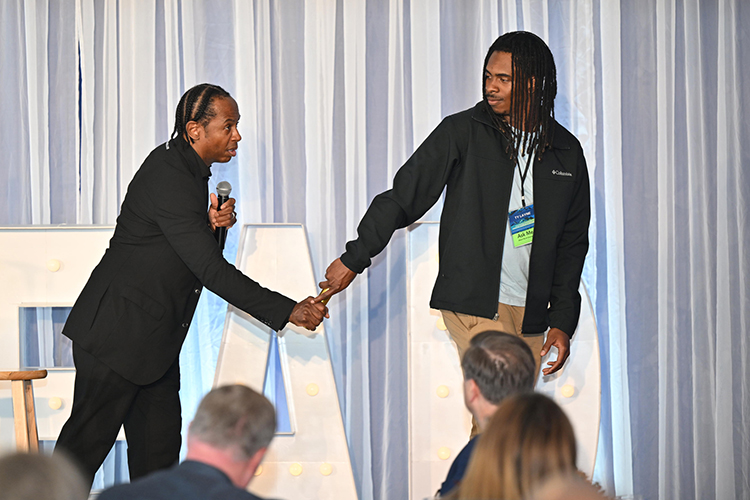 Internationally known educator, author and keynote speaker Adolph “Doc” Brown, left, passes a golden baton to Middle Tennessee State University management and leadership major Ty Layne of Fayetteville, Tenn., as part of an illustration at the 2024 Leadership Summit hosted Oct. 25 by the Jones College of Business at the Stones River Country Club in Murfreesboro. (MTSU photo by James Cessna)