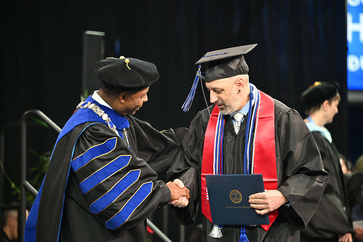 Wearing a red stole to signify his military service, a Middle Tennessee State University student veteran in the fall Class of 2024 shakes the hand of university President Sidney A. McPhee, who congratulates the newly minted graduate during the morning commencement ceremony held Saturday, Dec. 14, in Murphy Center on campus in Murfreesboro, Tenn. Nearly 1,600 graduates received their degrees. (MTSU photo by Cat Curtis Murphy)