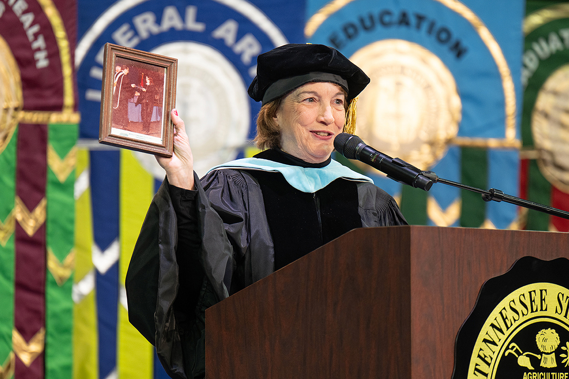 Middle Tennessee State University’s 2024 Distinguished Alumni Award recipient Peggy Chabrian, a longtime aviation enthusiast and educator, shows her official MTSU graduation photo from fall 1980 with the fall Class of 2024 graduating class during the morning commencement ceremony held Dec. 14 inside Murphy Center on campus in Murfreesboro, Tenn. MTSU presented nearly 1,600 degrees to undergrad and graduate students during morning and afternoon ceremonies. (MTSU photo by Cat Curtis Murphy)