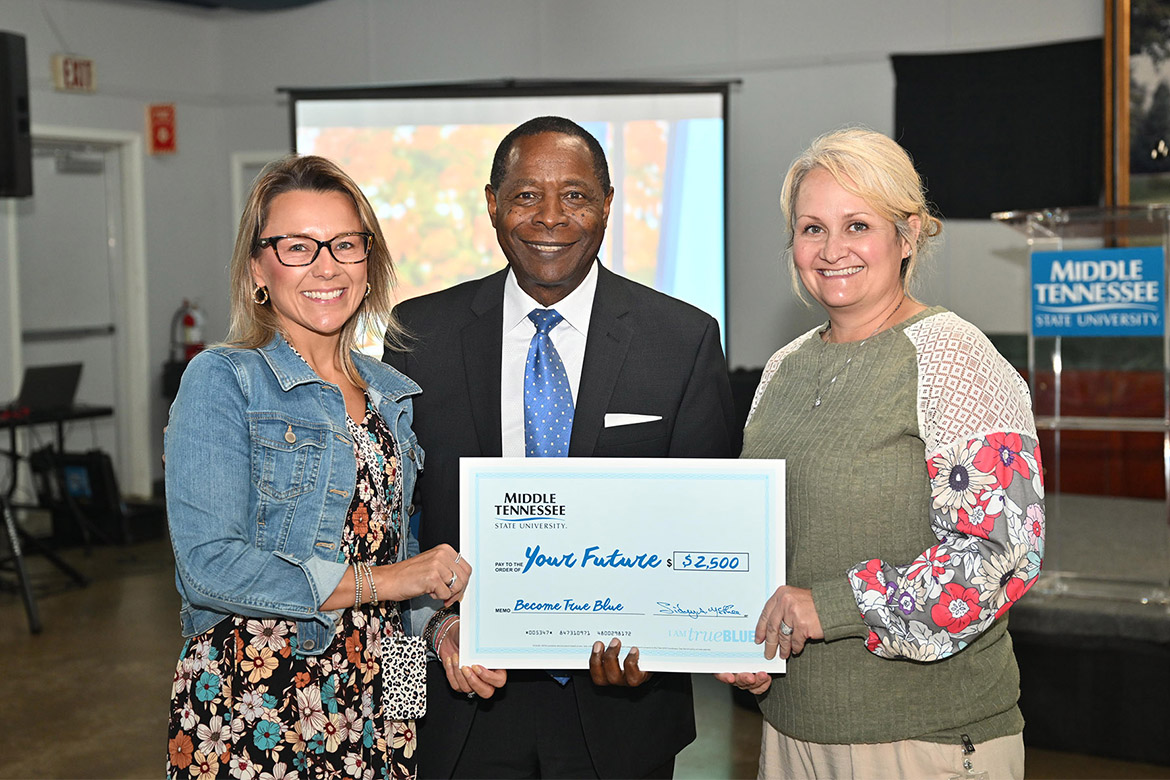 Middle Tennessee State University President Sidney A. McPhee, center, presents a $2,500 student scholarship to Moore County High School Assistant Principal Celina Mears, left, and school counselor Amy Kimbrough, at the 2025 True Blue Tour kickoff luncheon for counselors held Tuesday, Sept. 16, at the Blue Ribbon Circle Club in Shelbyville, Tenn. Moore County was one of 10 schools awarded scholarships to disperse to deserving students who plan to attend MTSU. (MTSU photo by James Cessna)
