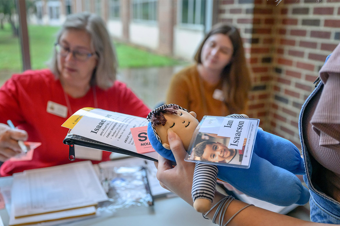 Community volunteers Jolene Radnoti, Read To Succeed director, background at left, and Brittany Satinover, UT/TSU Extension agent, participate in a poverty simulation held recently at Middle Tennessee State University in Murfreesboro, Tenn. In the foreground, a student is assigned the character of a little boy, simulated by a doll, who is accompanied by his parent at a health department appointment. (MTSU photo by J. Intintoli)