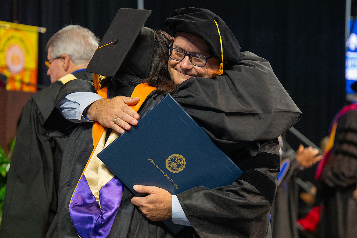 Middle Tennessee State University doctoral recipient Andrew Oppmann, vice president for marketing and communications, receives a congratulatory hug from a colleague during the fall commencement morning ceremony held Saturday, Dec. 13, in Murphy Center on the MTSU campus in Murfreesboro, Tenn. (MTSU photo by Cat Curtis Murphy)