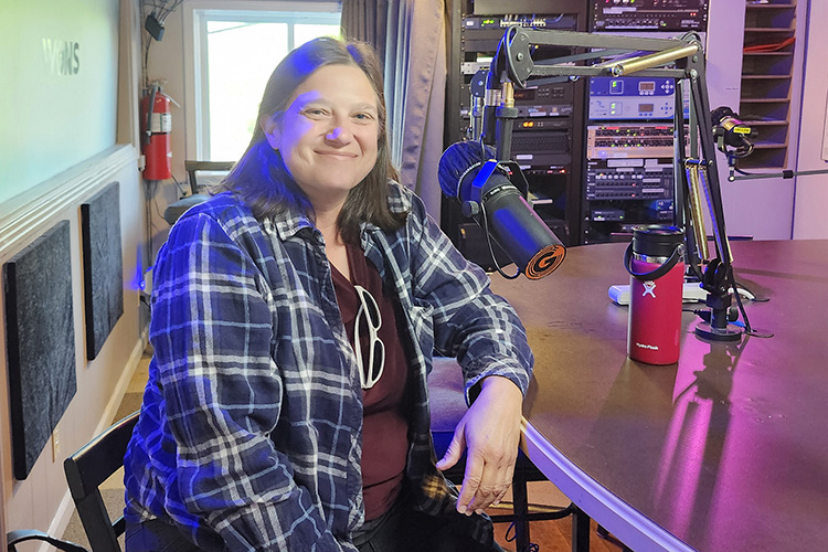 Woman in radio station studio seated behind microphone.