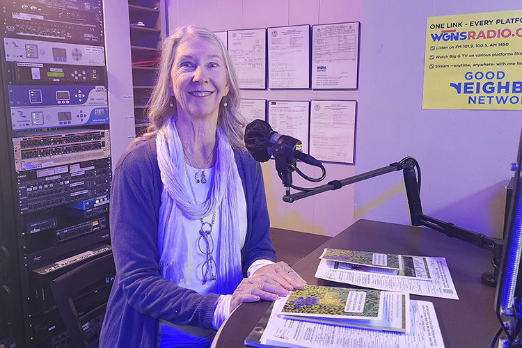 Woman in radio station studio seated behind microphone.