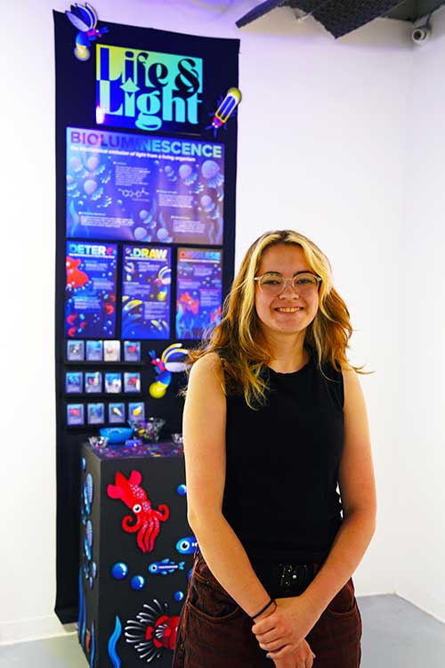 Lila Gordon, a senior graphic design major at Middle Tennessee State University, stands in front of her senior showcase graphic design project in the Todd Art Gallery, April 27, 2026. (MTSU photo by Mike Davis)