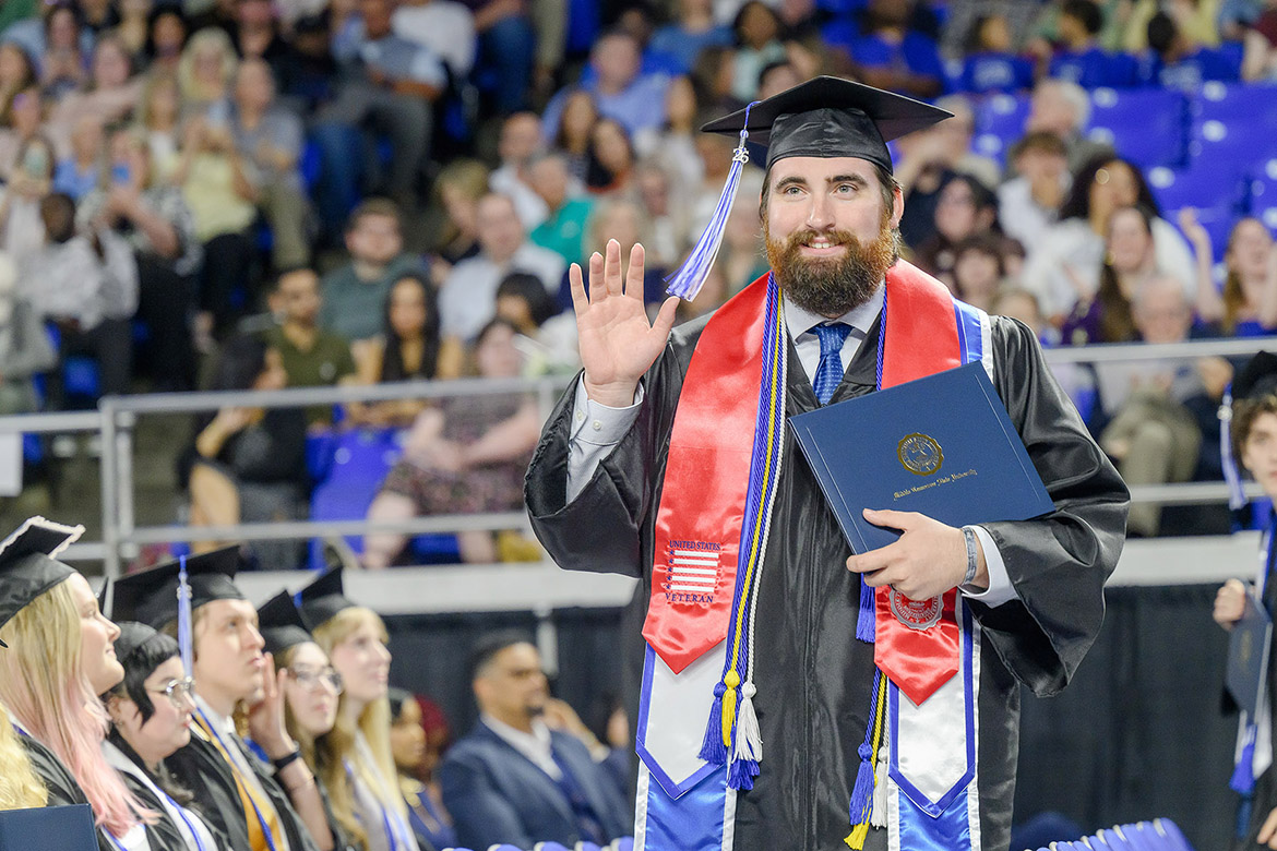 Wearing the special red stole designating his status as a student veteran, a Class of 2026 graduate waves to supporters during the spring commencement ceremony held Saturday morning, May 9, inside Murphy Center at Middle Tennessee State University in Murfreesboro, Tenn. (MTSU photo by J. Intintoli)
