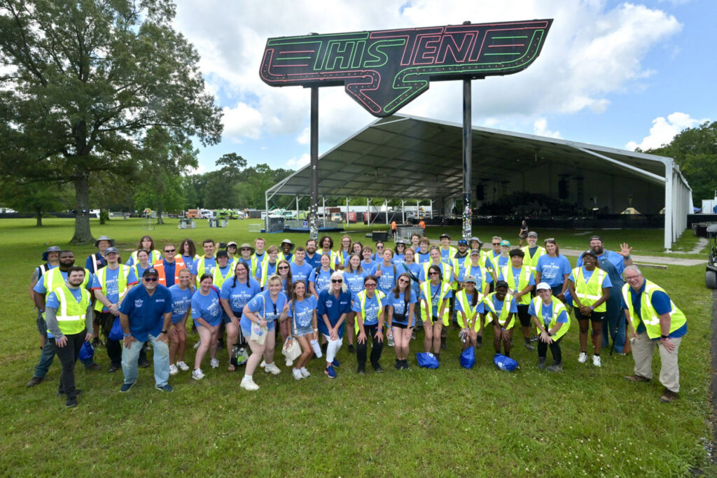 Large group of MTSU students, faculty and staff posing for group photo with large "This Tent" sign behind them at Bonnaroo site.