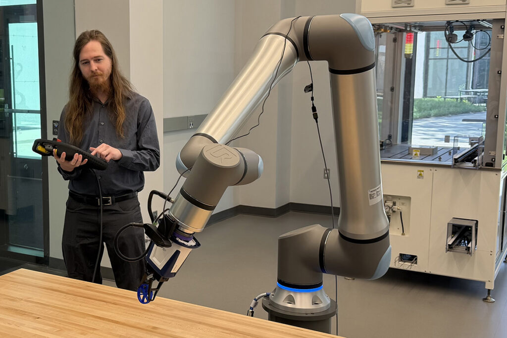 Matthew Crist, left, director of Electronics Labs in the Engineering Technology Department at Middle Tennessee State University in Murfreesboro, Tenn., demonstrates one of the robotic arms in the Applied Engineering Building used to train students in the mechatronics engineering program. (MTSU photo)