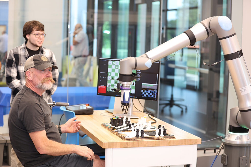 This undated photo shows a robotic arm preparing to move chess pieces as two students observe. Such equipment is available in the Applied Engineering Building at Middle Tennessee State University in Murfreesboro, Tenn., and is used to train Engineering Technology students pursuing mechatronics engineering. (MTSU photo)