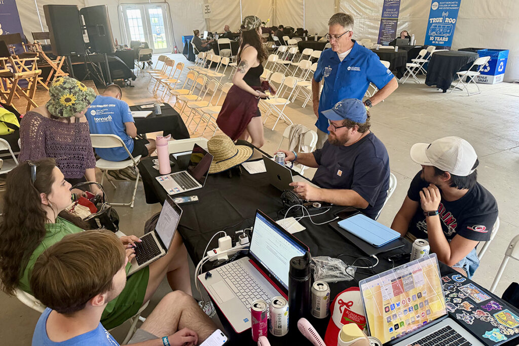 Mark Byrnes, standing top right, the provost at Middle Tennessee State University in Murfreesboro, Tenn., observes MTSU journalism students covering this year’s Bonnaroo Music and Arts Festival held June 11-14, 2026, in Manchester, Tenn. The students were led by assistant journalism professor Matt Leimkuehler, seated second from right. (MTSU photo by Andrew Oppmann)