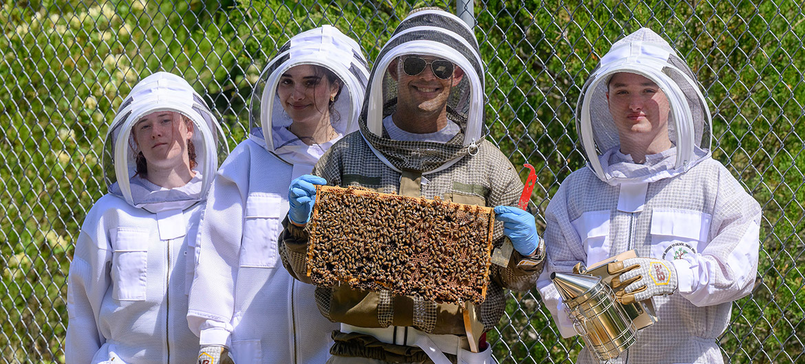 Manuel Giannoni-Guzmán, assistant professor of biology at Middle Tennessee State University in Murfreesboro, Tenn., holds up a beehive frame laden with honeybees at his outdoor lab located on the MTSU Small Farm facility in Lascassas, Tenn. Researchers on site at the MTSU Bee Lab are, from left, Mckenna Layman, a biochemistry major from Kodak, Tenn.; alumna Noor Obeissy, a 2025 biology graduate from Murfreesboro; Giannoni-Guzmán; and Collin Clark, a graduate student from Mt. Juliet, Tenn. (MTSU photo by J. Intintoli)