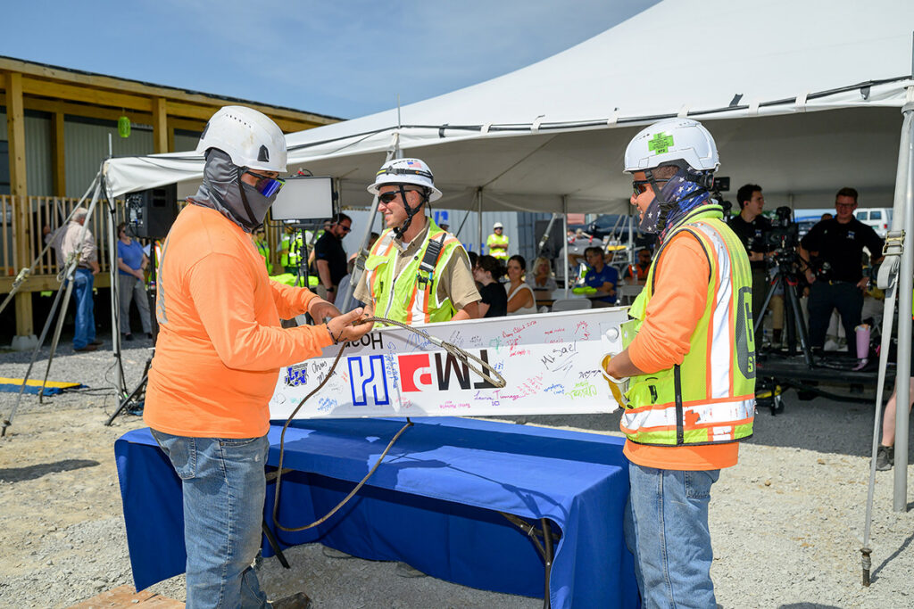 Three workers with Hoar Construction prepare the ceremonial beam to be lifted as part of the topping-out ceremony held Tuesday, July 21, 2026, for the Middle Tennessee State University Aerospace Department’s $62 million flight training center under construction at the Shelbyville, Tenn., Municipal Airport. The beam was later placed at the highest point of the 52,000-square-foot structure. (MTSU photo by J. Intintoli)