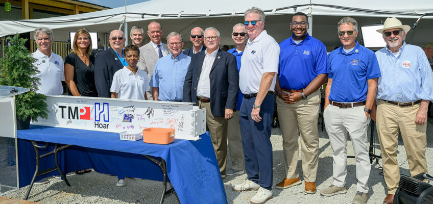Representatives from the Middle Tennessee State University Board of Trustees and other MTSU officials join elected officials from the city of Shelbyville, Tenn., for a group photo with the ceremonial beam at the topping-out ceremony held Tuesday, July 21, 2026, for the MTSU Aerospace Department’s $62 million flight training center under construction at the Shelbyville Municipal Airport. (MTSU photo by J. Intintoli)