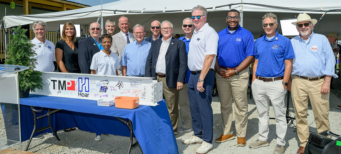 Representatives from the Middle Tennessee State University Board of Trustees and other MTSU officials join elected officials from the city of Shelbyville, Tenn., for a group photo with the ceremonial beam at the topping-out ceremony held Tuesday, July 21, 2026, for the MTSU Aerospace Department’s $62 million flight training center under construction at the Shelbyville Municipal Airport. (MTSU photo by J. Intintoli)
