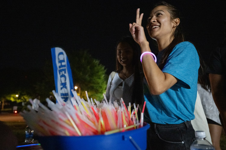 Students smile and hold up peace signs as they choose from a bucket of glow-in-the-dark bracelets.