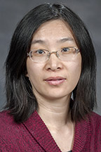 A woman with light tan skin and dark hair wearing frameless glasses and a maroon sweater looks at the camera. 