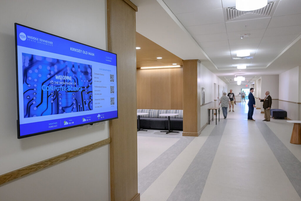 A monitor on the wall of Kirksey Old Main reads "Welcome to the Department of Computer Science."
