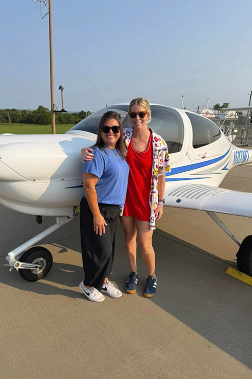 Two teachers stand in front on a small white and blue plane on a tarmac in Dayton, Tennessee.
