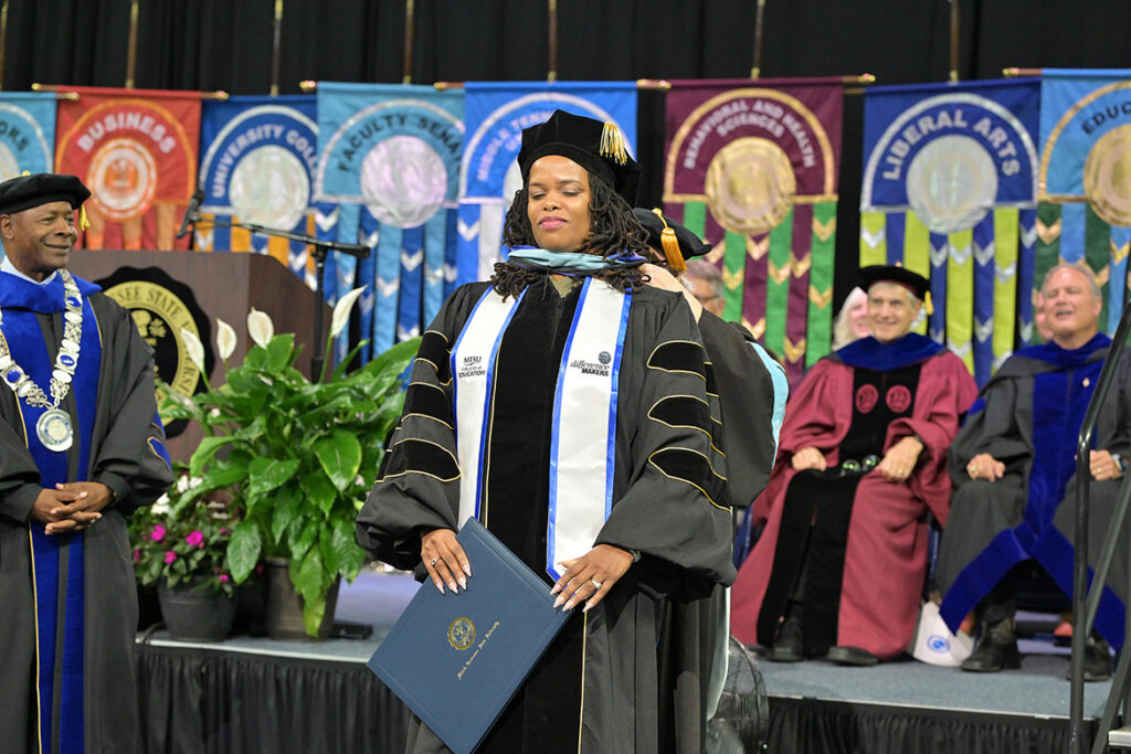 Middle Tennessee State University summer graduate and doctoral recipient Danielle Rochelle, specialist in the Office of Student Care and Conduct, is hooded by her professor Kim Godwin during the summer commencement ceremony held Saturday, Aug. 8, 2026, inside Murphy Center on campus in Murfreesboro, Tenn. (MTSU photo by James Cessna)