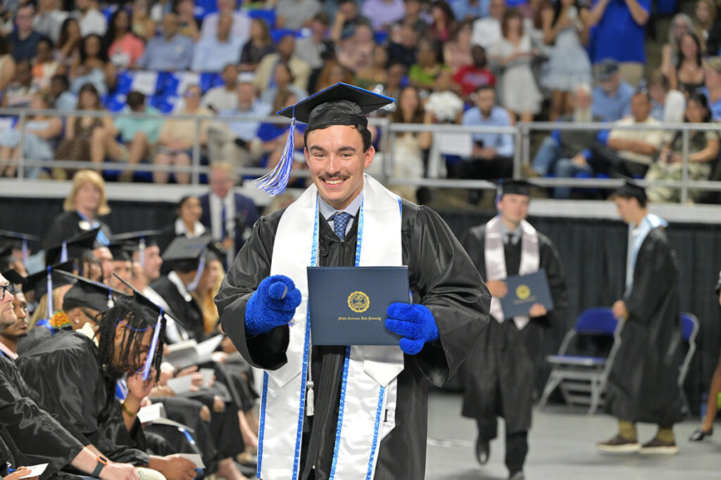 A proud Middle Tennessee State University graduate donning blue furry hands (a friend of mascot Lightning, perhaps?) is all smiles after receiving his degree during the summer commencement ceremony held Saturday, Aug. 8, 2026, inside Murphy Center on campus in Murfreesboro, Tenn. (MTSU photo by James Cessna)