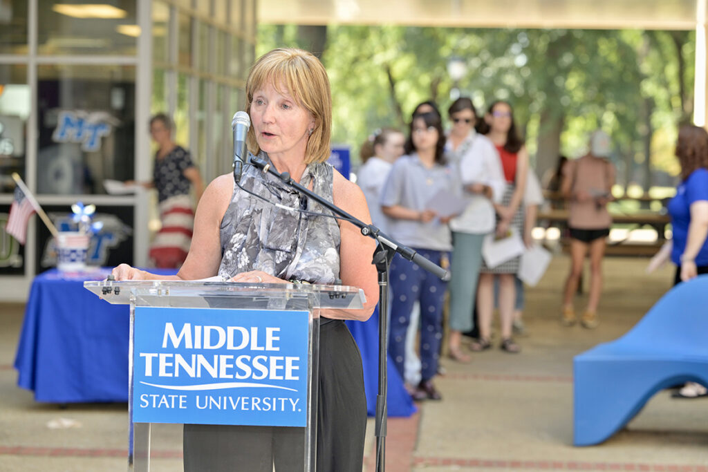 A woman reading a document standing behind a lectern outside.