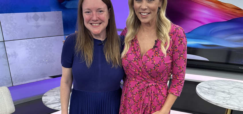 Two women smiling standing beside each other on TV studio set.