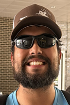 Bearded man wearing sunglasses and a baseball cap smiling.