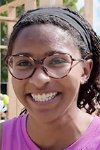 A with brown skin, dark hair and glasses smiles at the camera.