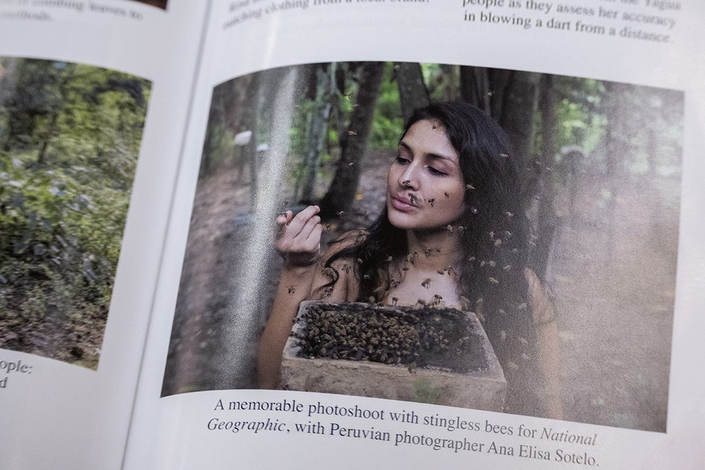A book lays open with a picture of a women with dark hair and tan skin covered in stingless Amazonian bees.