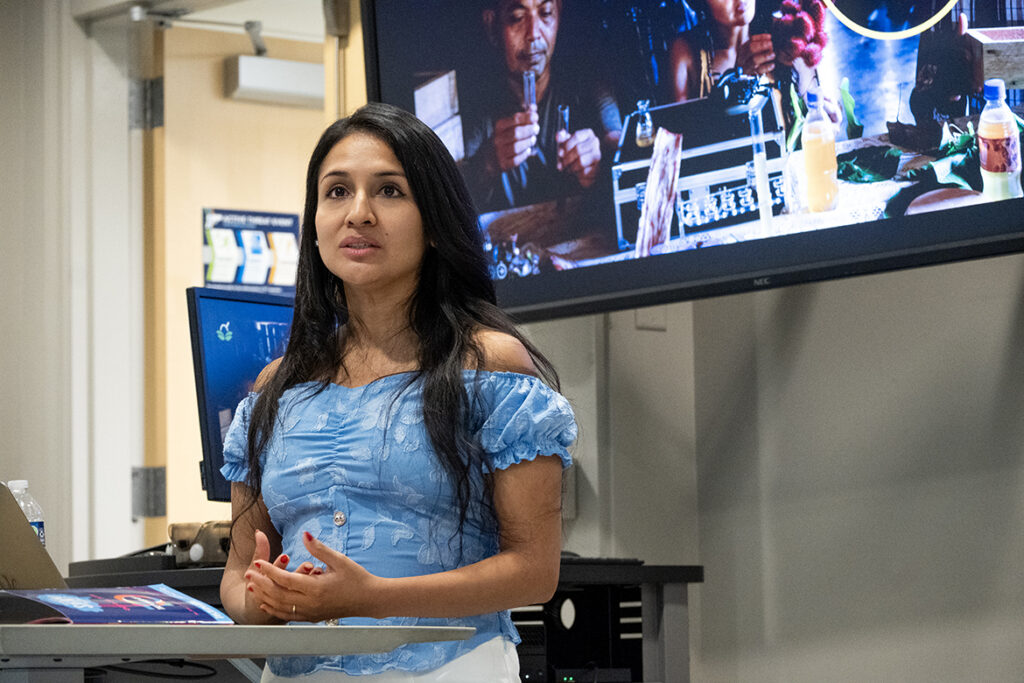A woman with tan skin and long dark hair stands behind a podium.