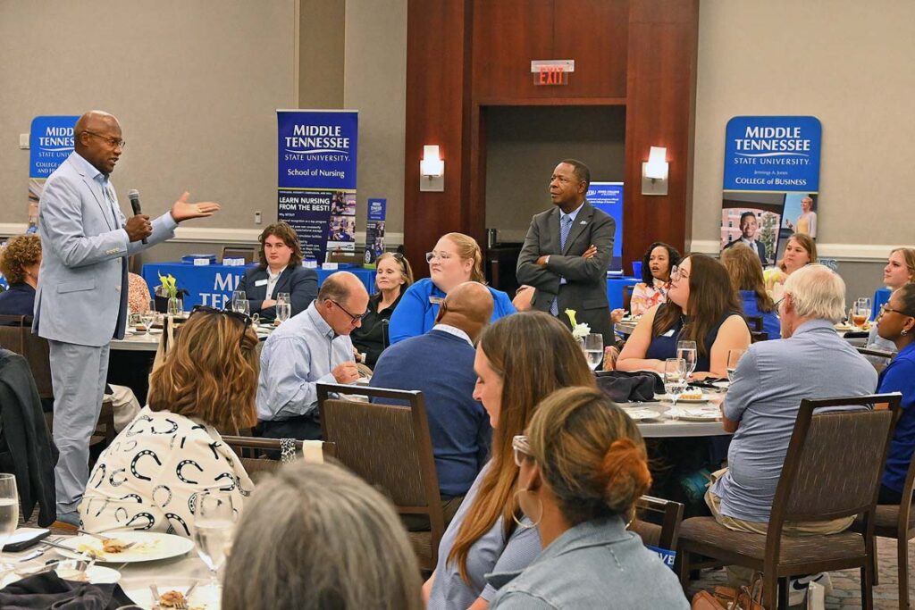 Sidney A. McPhee, standing at right, president of Middle Tennessee State University in Murfreesboro, Tenn., listens to alumnus Keith Cromartie of Huntsville, Ala., tell the crowd of high school and community college career counselors gathered at The Westin Huntsville about his life-changing experiences at MTSU during the True Blue Tour recruitment stop held Wednesday, Oct. 14, in Huntsville. (MTSU photo by Nancy DeGennaro)